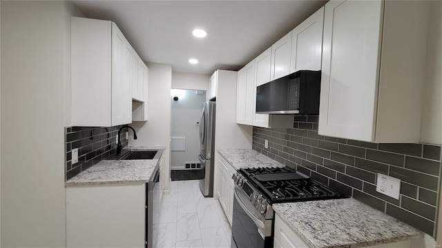 kitchen with a sink, white cabinetry, marble finish floor, appliances with stainless steel finishes, and light stone countertops