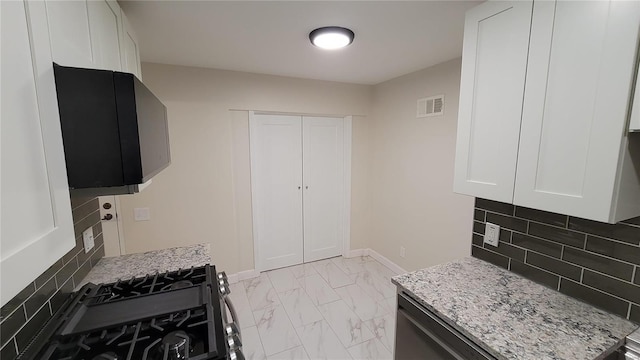 kitchen with tasteful backsplash, visible vents, white cabinets, light stone counters, and marble finish floor