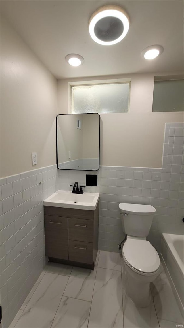 bathroom featuring toilet, marble finish floor, a tub to relax in, and vanity