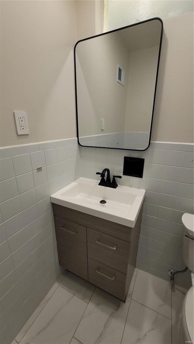 half bath with tile walls, marble finish floor, vanity, and toilet