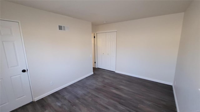 unfurnished room featuring dark wood-style flooring, visible vents, and baseboards