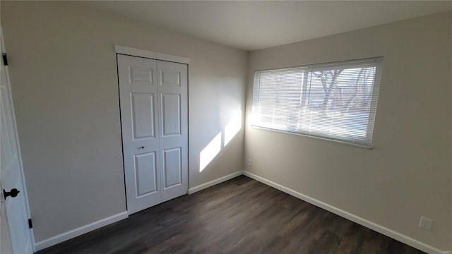 unfurnished bedroom with a closet, baseboards, and dark wood-style flooring