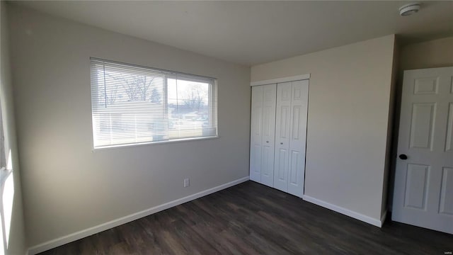 unfurnished bedroom featuring a closet, baseboards, and dark wood-type flooring