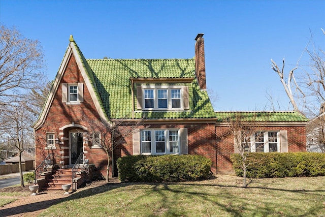 tudor house featuring a front yard, brick siding, and a chimney