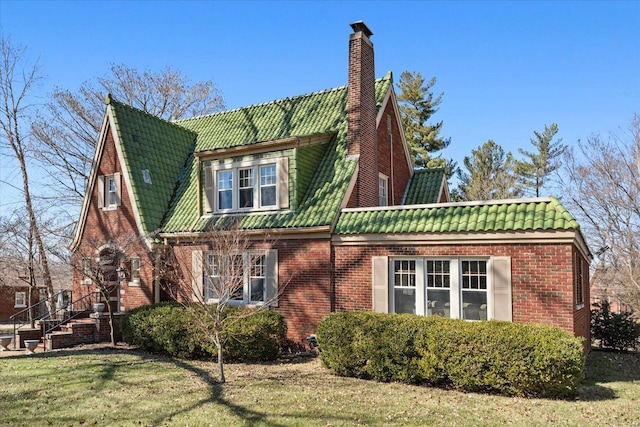 view of side of home featuring brick siding, a tile roof, a chimney, and a yard