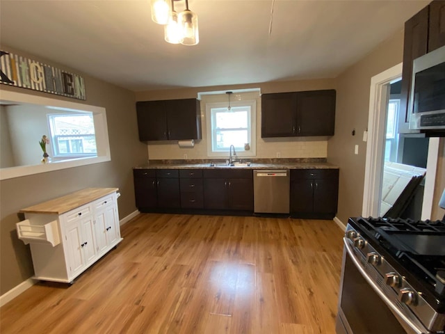 kitchen with light wood finished floors, stainless steel appliances, a sink, dark brown cabinets, and baseboards