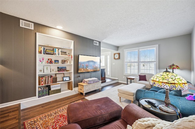 living area featuring a textured ceiling, wood finished floors, visible vents, and wooden walls