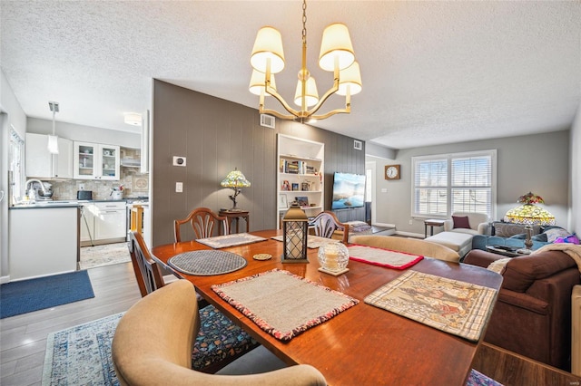 dining space with visible vents, a textured ceiling, an inviting chandelier, and wood finished floors