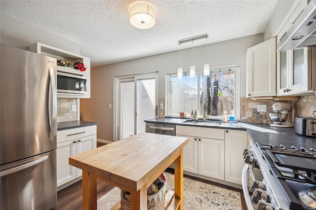 kitchen featuring stainless steel appliances, dark countertops, a wealth of natural light, and white cabinets