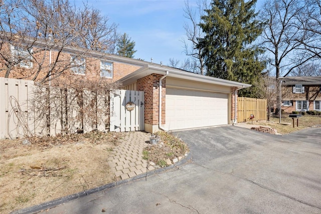 view of front of home featuring brick siding, an attached garage, fence, and aphalt driveway