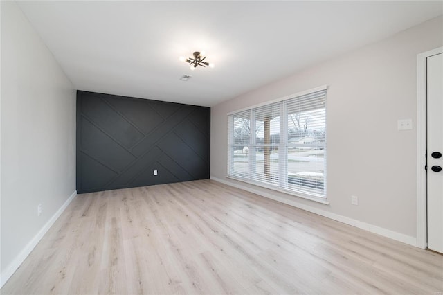 spare room featuring an accent wall, baseboards, and wood finished floors