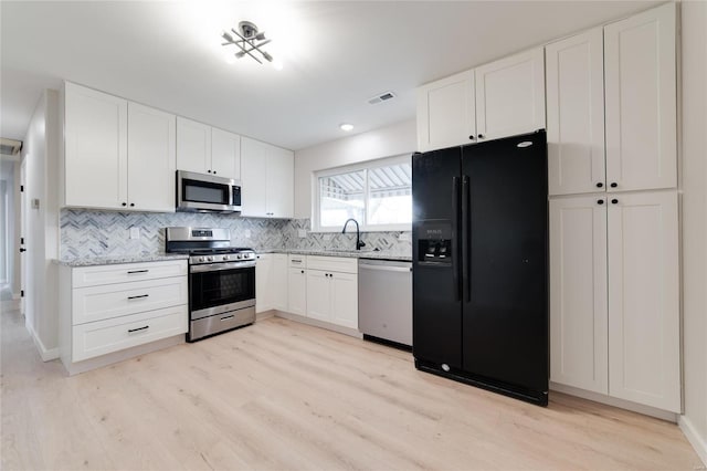 kitchen with appliances with stainless steel finishes, light wood-type flooring, visible vents, and tasteful backsplash