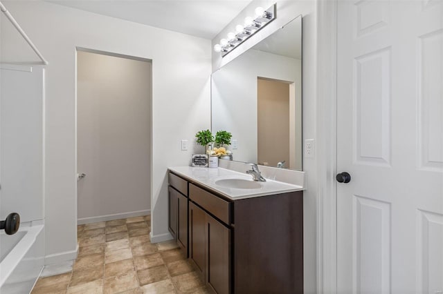 full bath featuring a tub, stone finish floor, vanity, and baseboards