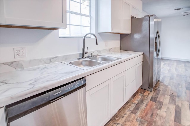 kitchen with light stone counters, wood finished floors, a sink, white cabinets, and appliances with stainless steel finishes