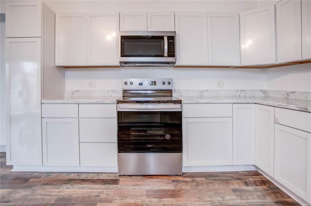 kitchen with appliances with stainless steel finishes, wood finished floors, white cabinetry, and light stone countertops