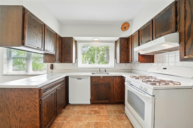kitchen with decorative backsplash, white appliances, stone finish floor, under cabinet range hood, and a sink