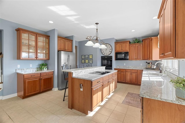 kitchen with black appliances, a sink, a kitchen island, brown cabinetry, and light stone countertops