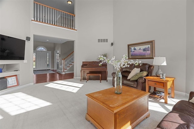 carpeted living area featuring visible vents, baseboards, a towering ceiling, and stairs