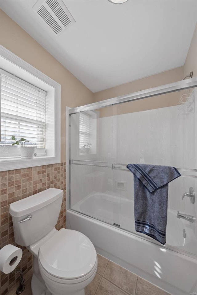 full bath featuring visible vents, shower / bath combination with glass door, tile patterned flooring, tile walls, and toilet