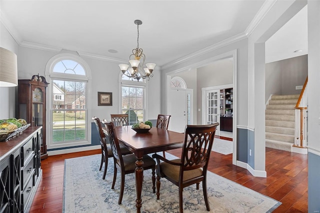 dining area with dark wood-type flooring, an inviting chandelier, ornamental molding, and stairs