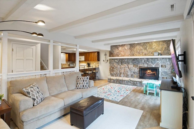 living area with visible vents, stairway, a stone fireplace, wood finished floors, and beamed ceiling