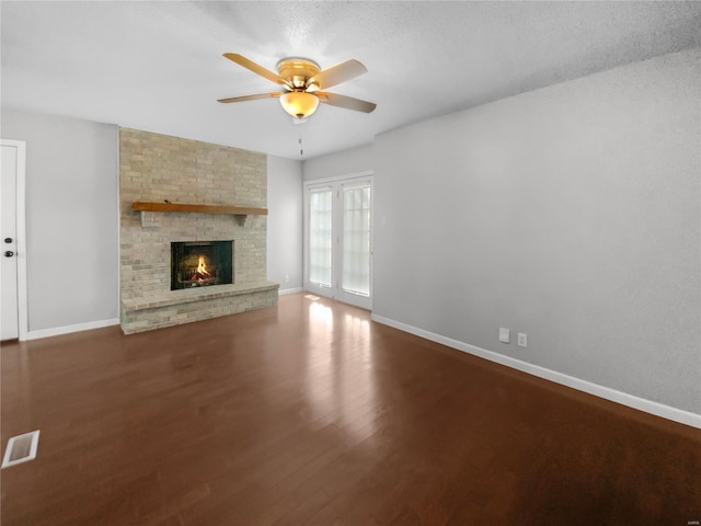 unfurnished living room featuring baseboards, visible vents, a ceiling fan, wood finished floors, and a brick fireplace