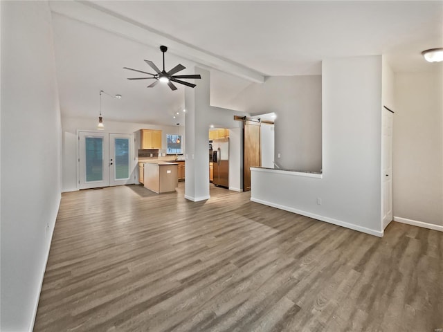 unfurnished living room with wood finished floors, lofted ceiling with beams, baseboards, and a barn door