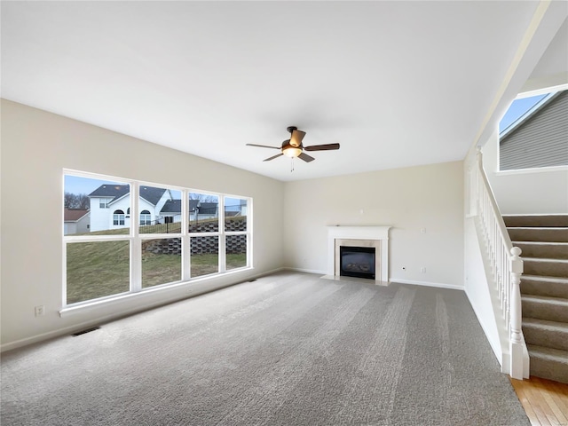 unfurnished living room featuring plenty of natural light, stairs, visible vents, and a fireplace with flush hearth