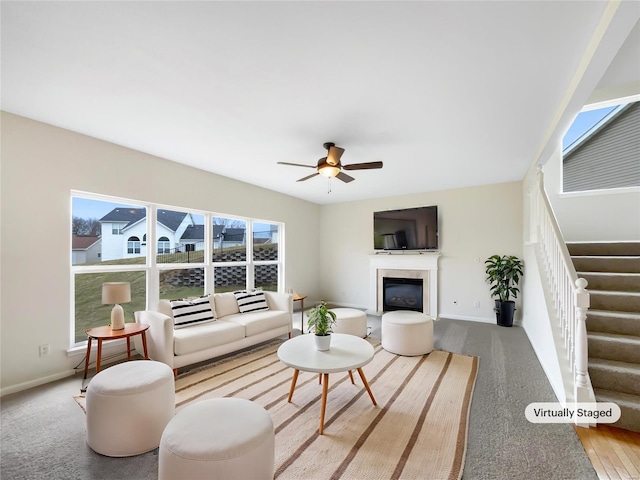 living room featuring stairs, ceiling fan, a glass covered fireplace, and baseboards