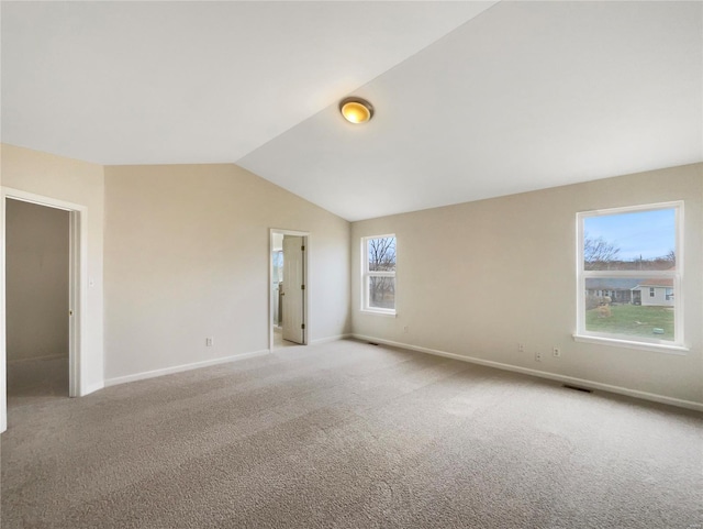 empty room featuring baseboards, visible vents, vaulted ceiling, and light colored carpet