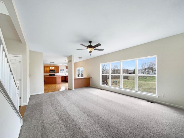 unfurnished living room with a ceiling fan, light carpet, baseboards, and stairs