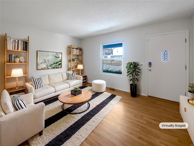 living room featuring light wood-type flooring, baseboards, and a textured ceiling