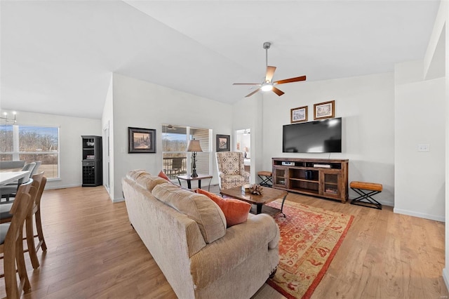 living area featuring baseboards, lofted ceiling, wood finished floors, and ceiling fan with notable chandelier