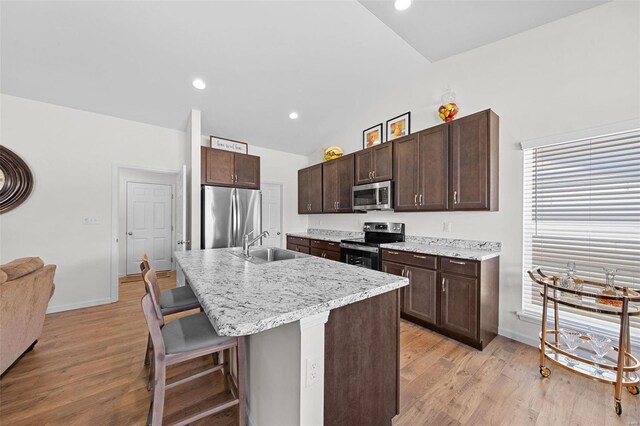 kitchen featuring a kitchen bar, light wood-style floors, appliances with stainless steel finishes, lofted ceiling, and dark brown cabinets