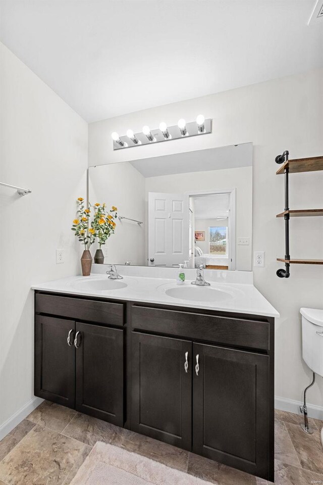 bathroom featuring double vanity, toilet, baseboards, and a sink