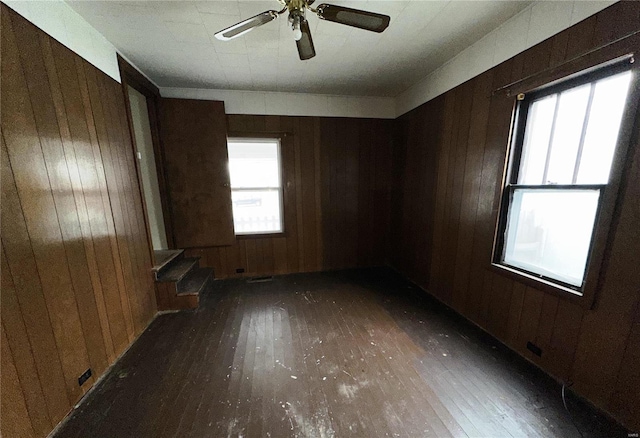 empty room featuring ceiling fan, wooden walls, stairway, and dark wood-type flooring