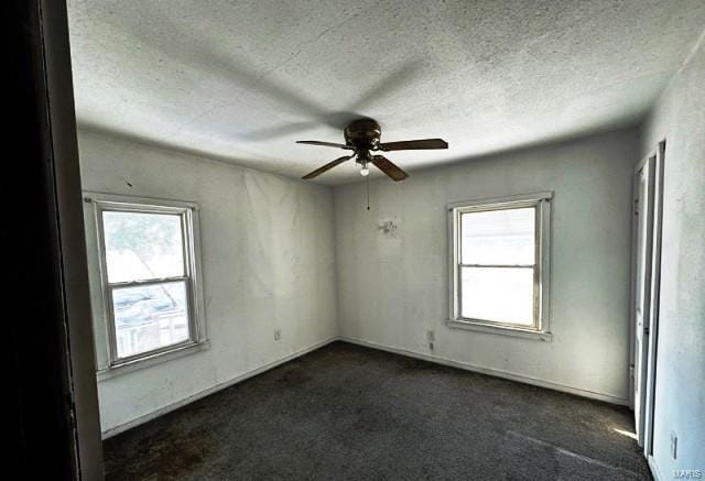 spare room featuring plenty of natural light, ceiling fan, a textured ceiling, and dark carpet