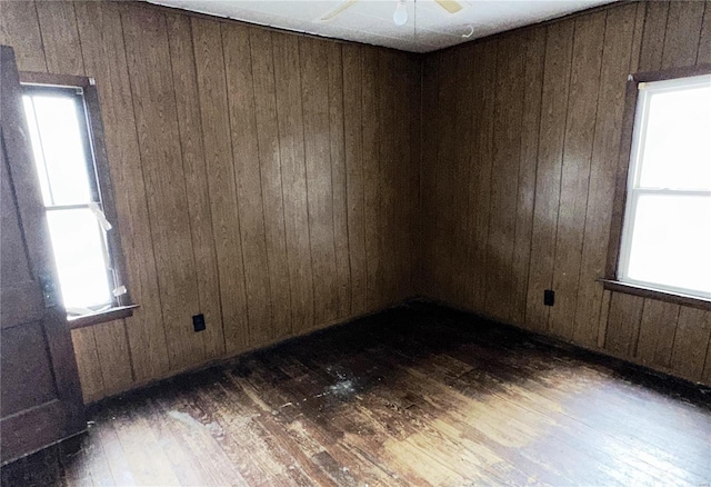 empty room featuring ceiling fan, wooden walls, and dark wood-type flooring