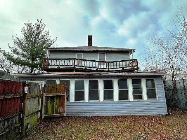 back of house with a balcony, a chimney, and fence