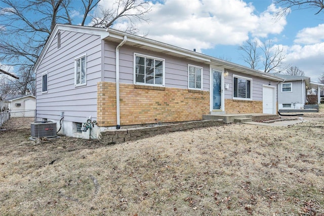 ranch-style house featuring an attached garage, fence, cooling unit, and brick siding