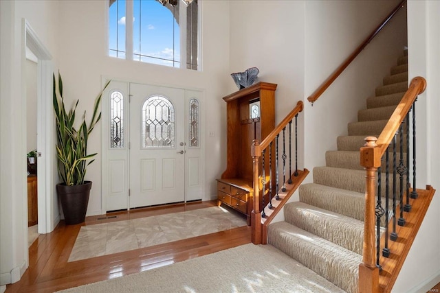 foyer entrance with a towering ceiling, light wood-style flooring, and stairway