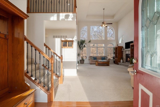 carpeted entrance foyer featuring a towering ceiling, a tray ceiling, a wealth of natural light, and a stone fireplace