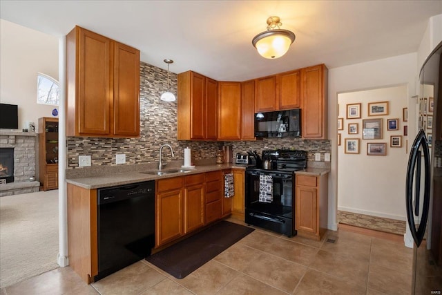 kitchen with black appliances, light countertops, a sink, and a stone fireplace