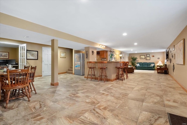 interior space featuring a breakfast bar area, freestanding refrigerator, open floor plan, a peninsula, and baseboards