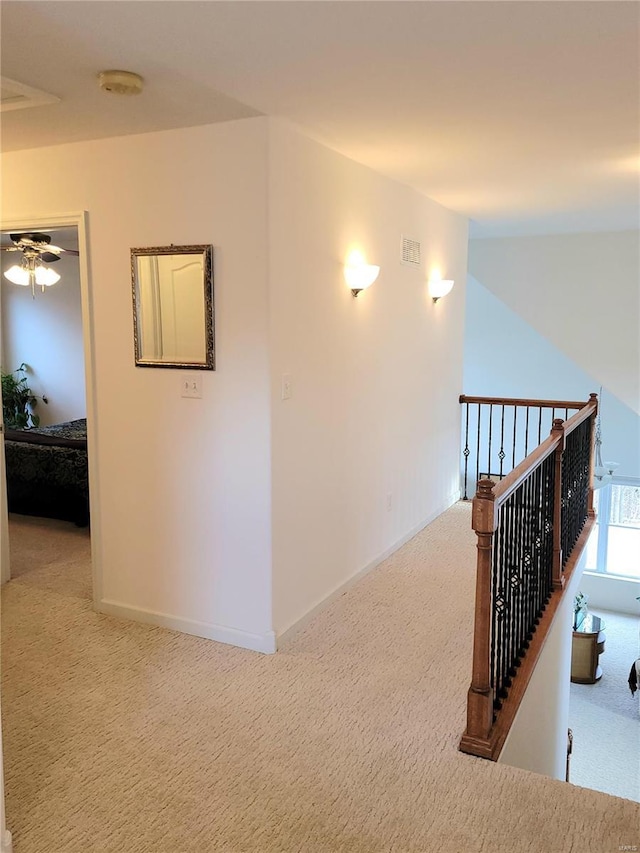 hall with light carpet, visible vents, and baseboards