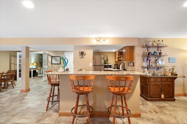 bar featuring freestanding refrigerator, indoor wet bar, a sink, and baseboards