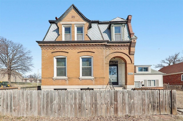 view of front facade featuring a fenced front yard, a high end roof, brick siding, and a chimney