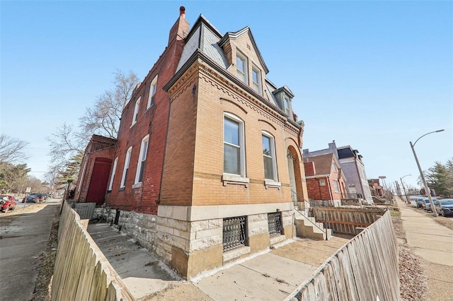 view of home's exterior with brick siding, fence, and a chimney