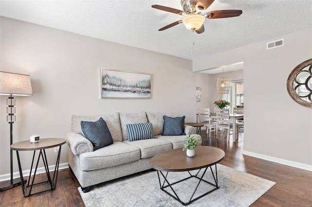 living area featuring dark wood-style flooring, visible vents, a ceiling fan, a textured ceiling, and baseboards