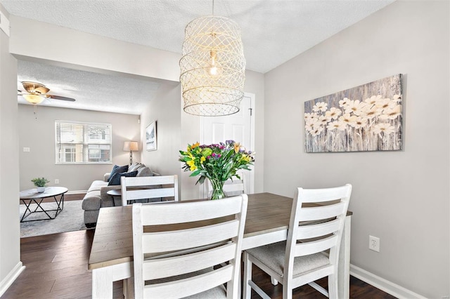 dining room with a textured ceiling, baseboards, dark wood-style flooring, and ceiling fan with notable chandelier